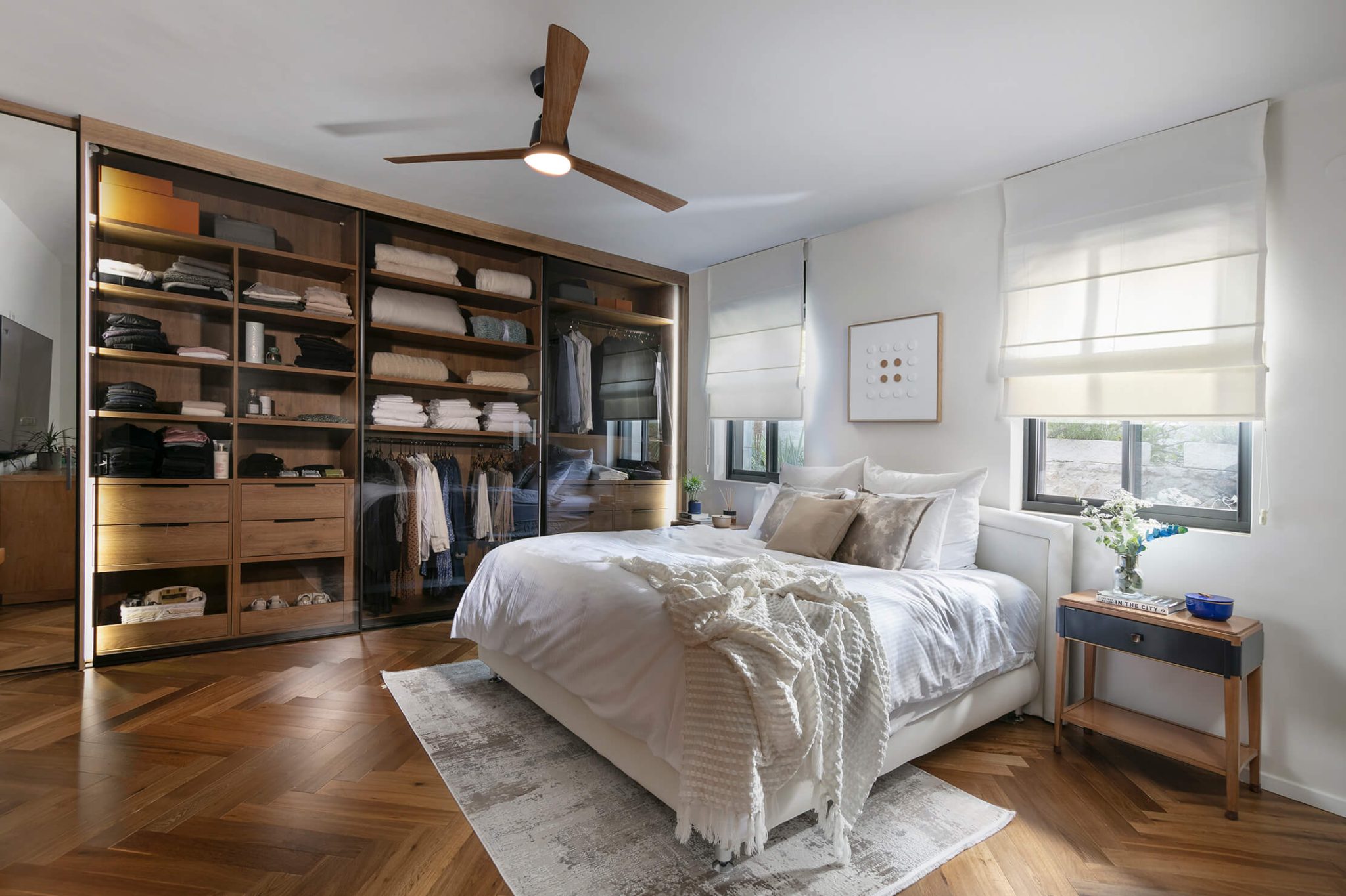 Master bedroom with a large king size bed in the middle of the room, with parquet flooring and a transperent wardrobe.