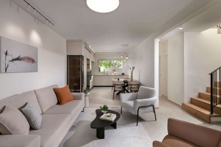 מבט מהסלון אל המטבח בבית פרטי בכוכב יאיר, חלל פתוח עם רצף עיצובי, תאורה טבעית והרמוניה בין אזורי המגורים