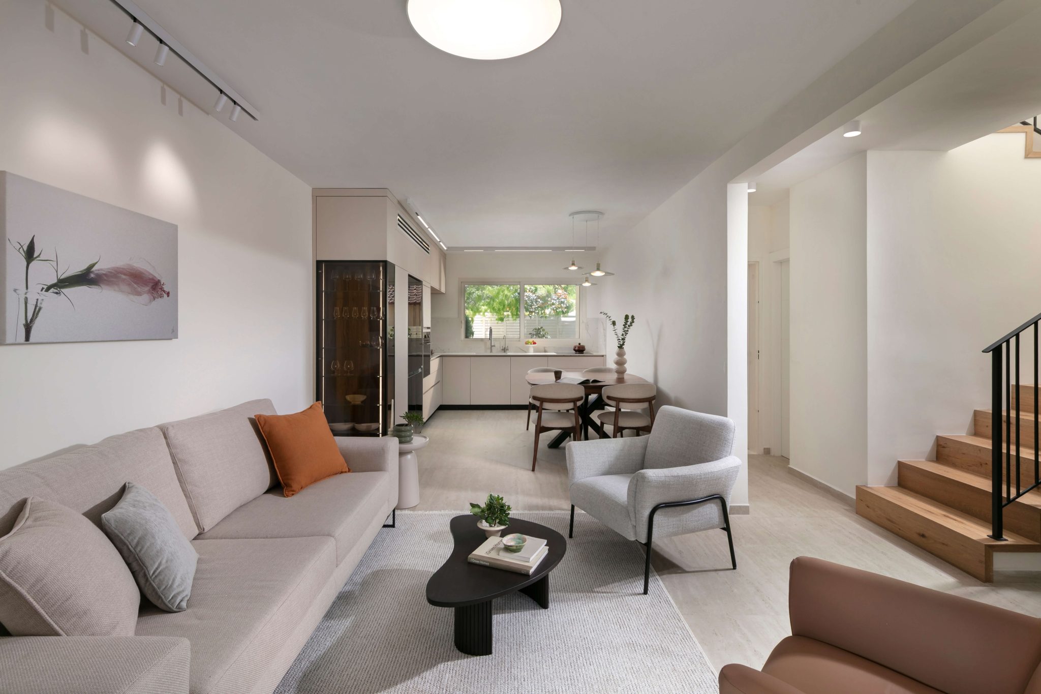 מבט מהסלון אל המטבח בבית פרטי בכוכב יאיר, חלל פתוח עם רצף עיצובי, תאורה טבעית והרמוניה בין אזורי המגורים